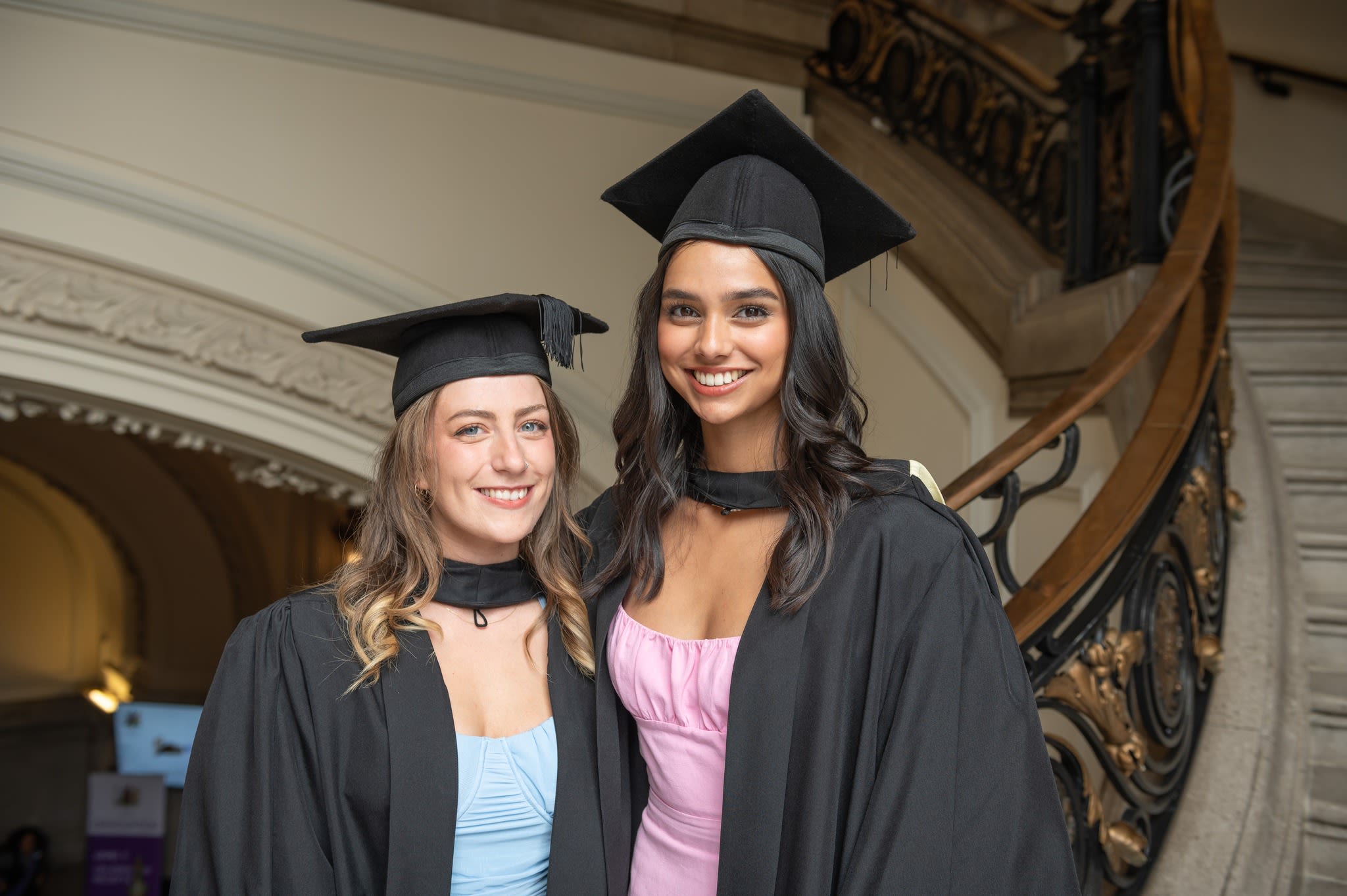 Two graduates smile on the stairs